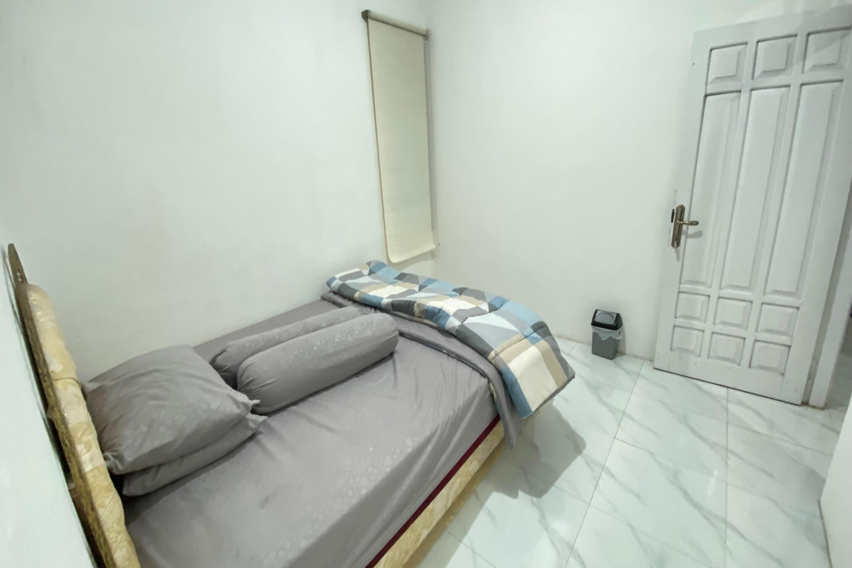 A small, clean room with a single bed, a white door, and a trash bin.