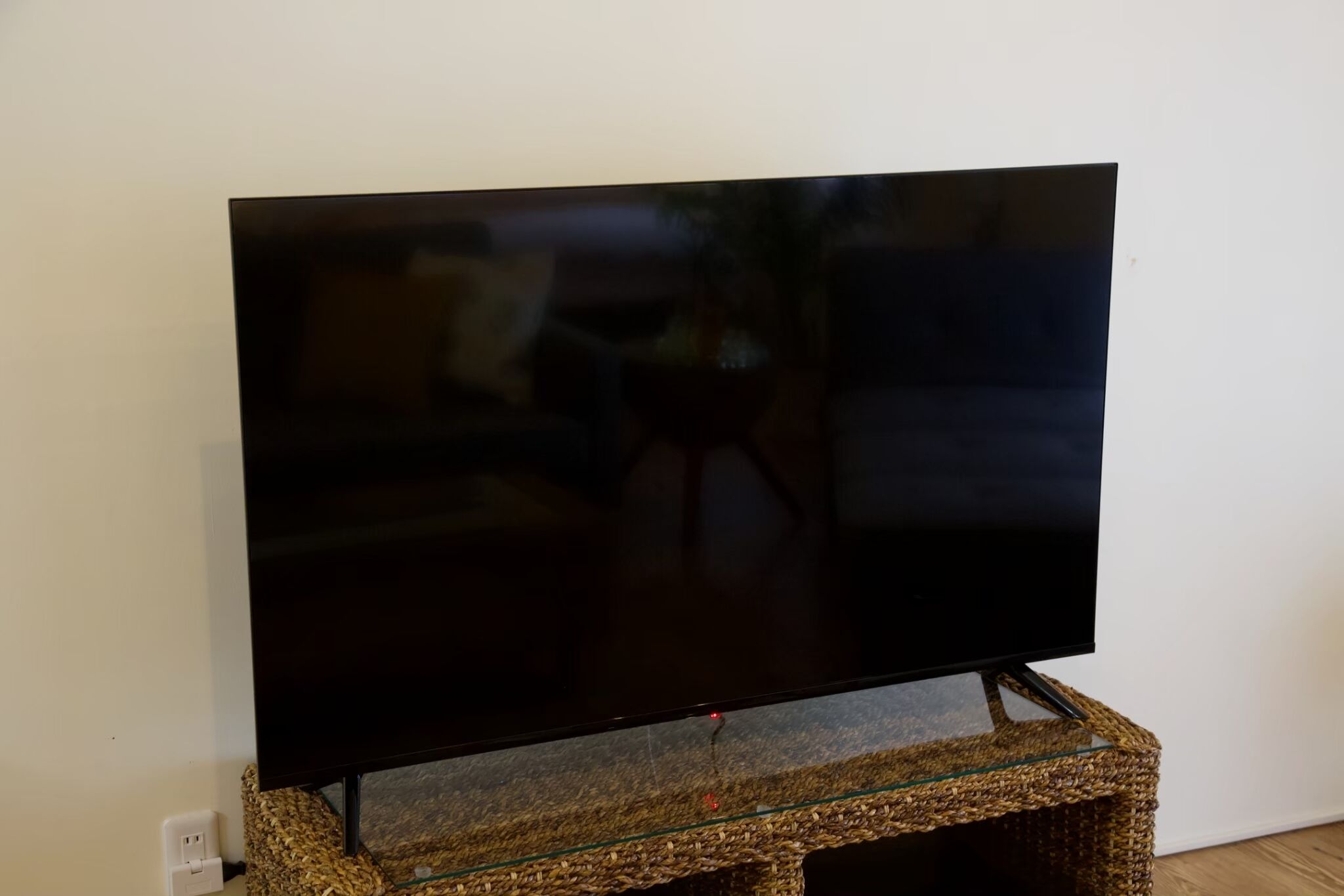 A flat-screen TV on a glass-top stand against a white wall.
