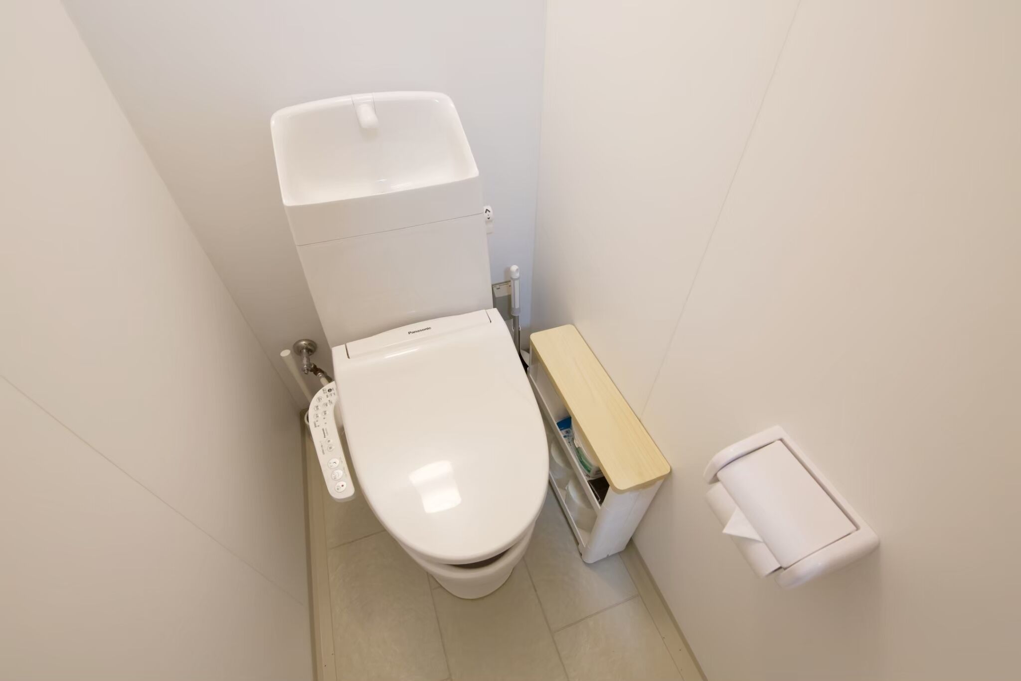 Ett litet, rent badrum med en vit toalett, ett träskåp och en vit papperskorg.