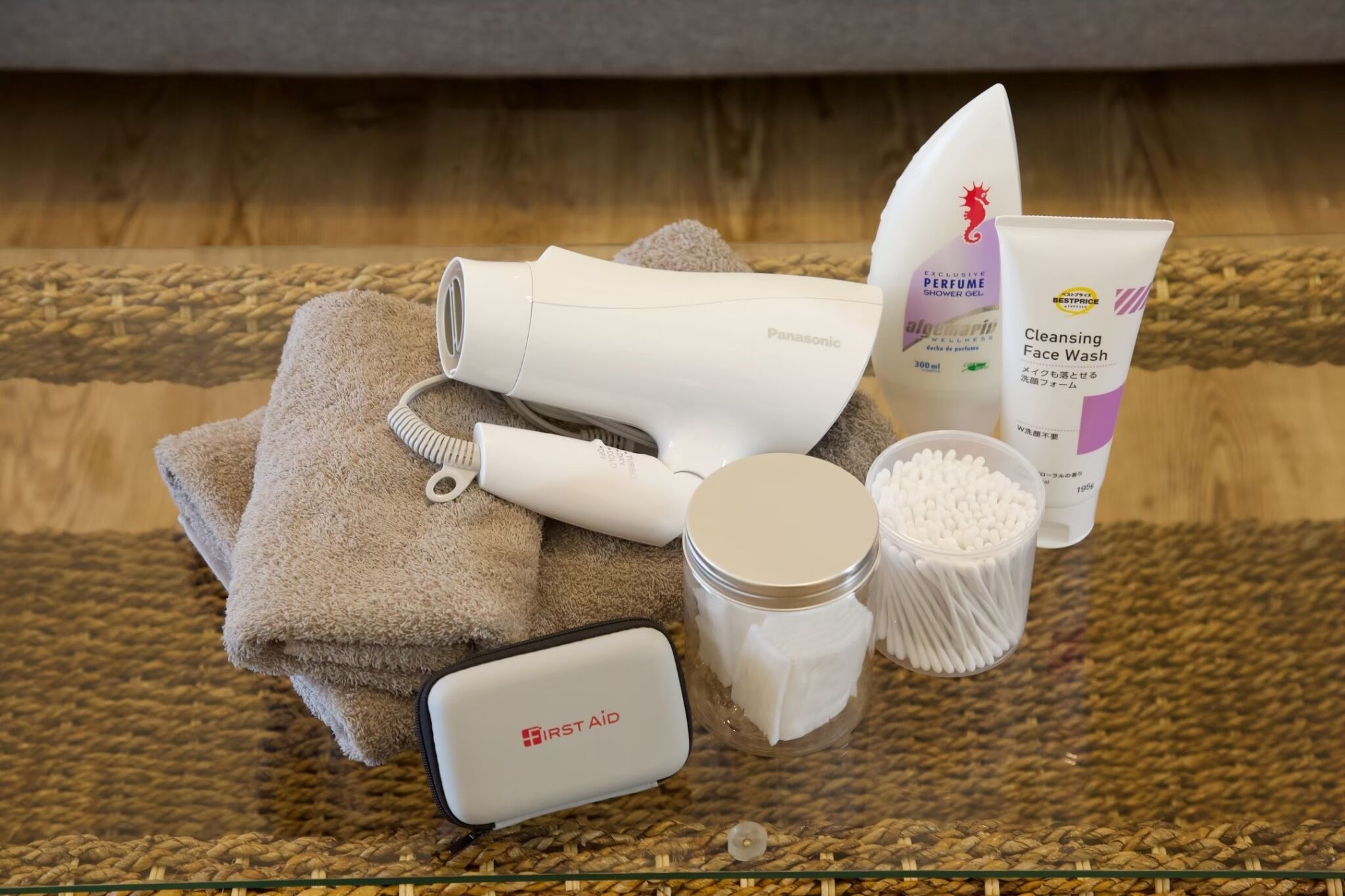 Uma toucador de banheiro com toalha, secador de cabelo, kit de primeiros socorros, um frasco de cotonetes e um produto de limpeza facial.