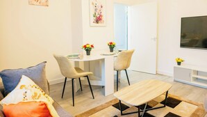 A modern living room with a dining area, a sofa, a coffee table, and a TV mounted on the wall. - Central Cardiff Cozy 2BR Near Stadium Shops Uni (Cardiff)