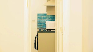 A compact kitchen with a microwave, stove, and blue-tiled backsplash. - Central Cardiff Cozy 2BR Near Stadium Shops Uni (Cardiff)
