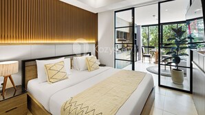 A modern bedroom with a large bed, wooden panel wall, and a view of the outdoors through a glass door. - Caraya by Kozystay - Nusa Dua (Nusa Dua)