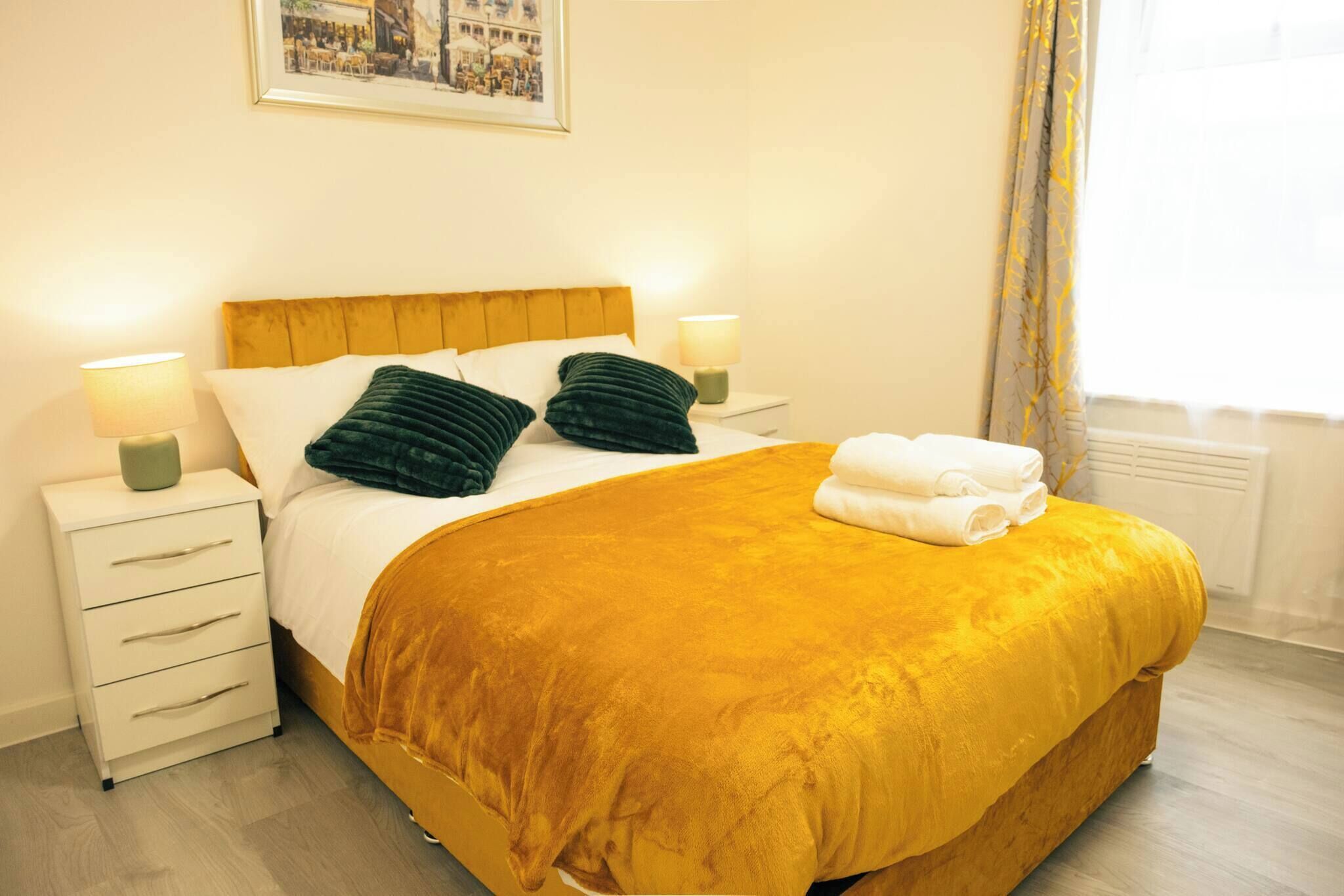 A hotel room with a bed, two bedside tables, a nightstand, a lamp, and a window with curtains.