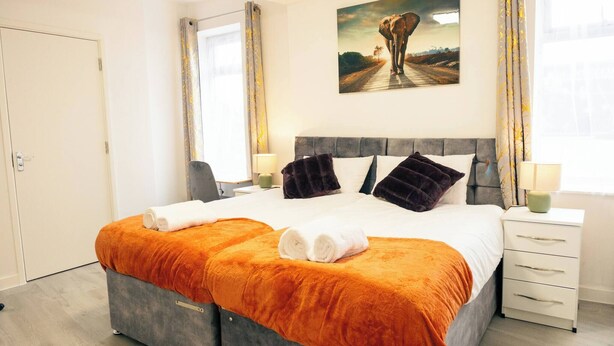 Ett hotellrum med en stor säng, ett sängbord, en liten avlastningsyta, en tavla på väggen och en dörr.