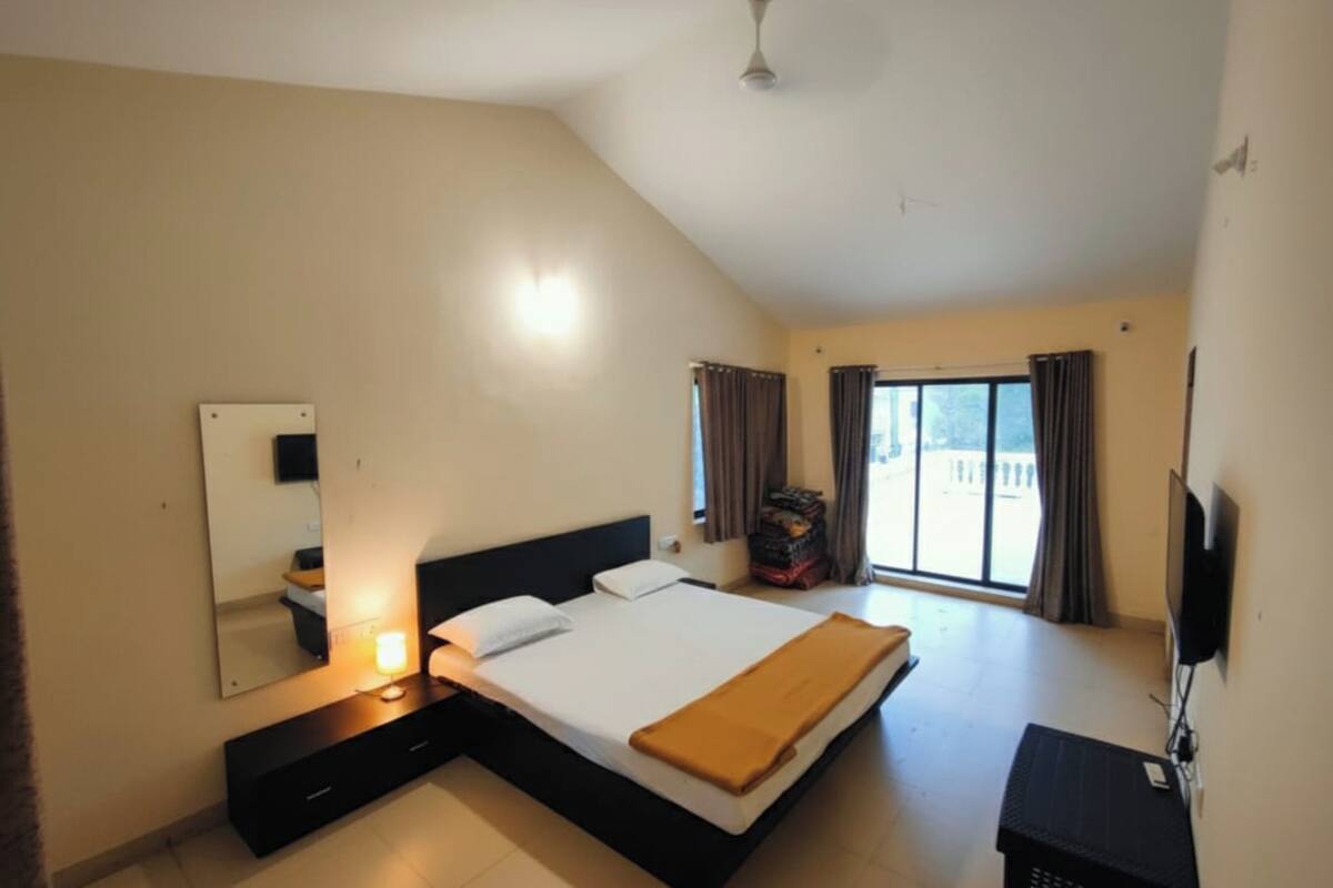 A bedroom with a bed, a bedside table, a TV, and a window with curtains.