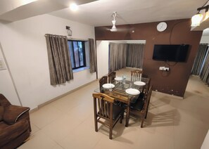 A dining area with a glass table, wooden chairs, and a television mounted on the wall. - Hifi Private Villa (Nagaon)