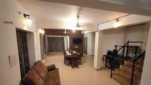 Uma sala ampla com um sofá marrom, uma mesa de jantar e uma escada.