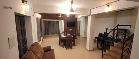 A spacious living area with a brown sofa, a dining table, and a staircase.