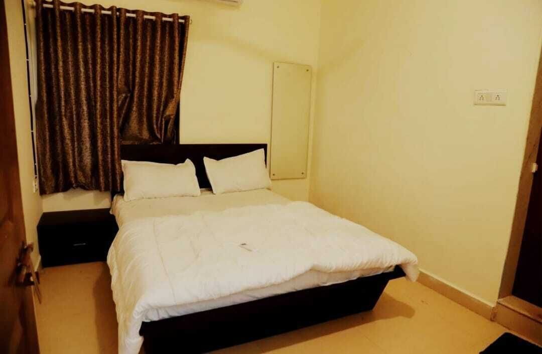A bedroom with a single bed, a nightstand, a dark headboard, and a curtain.
