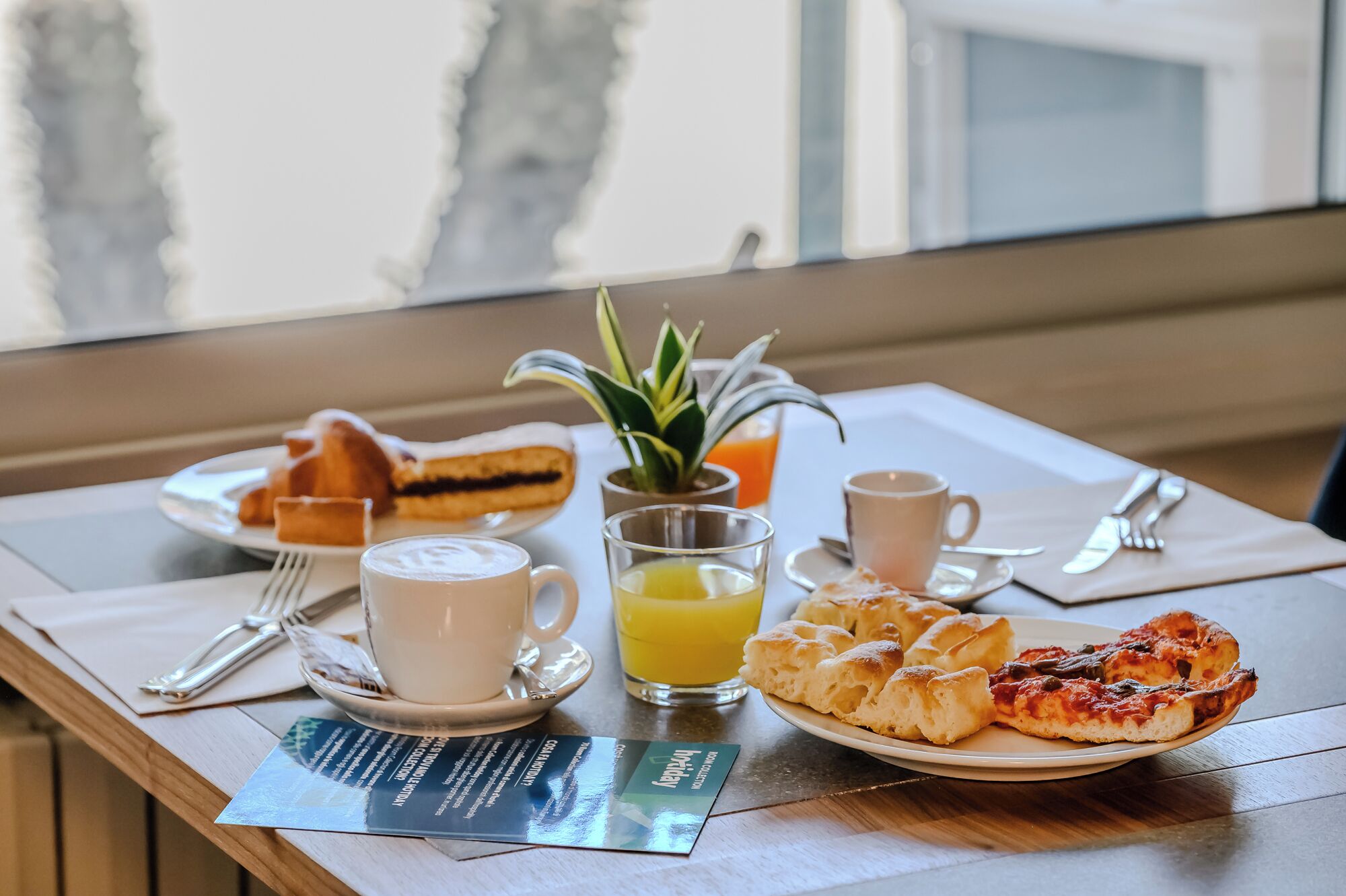 A breakfast setting with pastries, a glass of orange juice, a cup of coffee, and a small plant on the table.