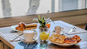 A breakfast setting with pastries, a glass of orange juice, a cup of coffee, and a small plant on the table.