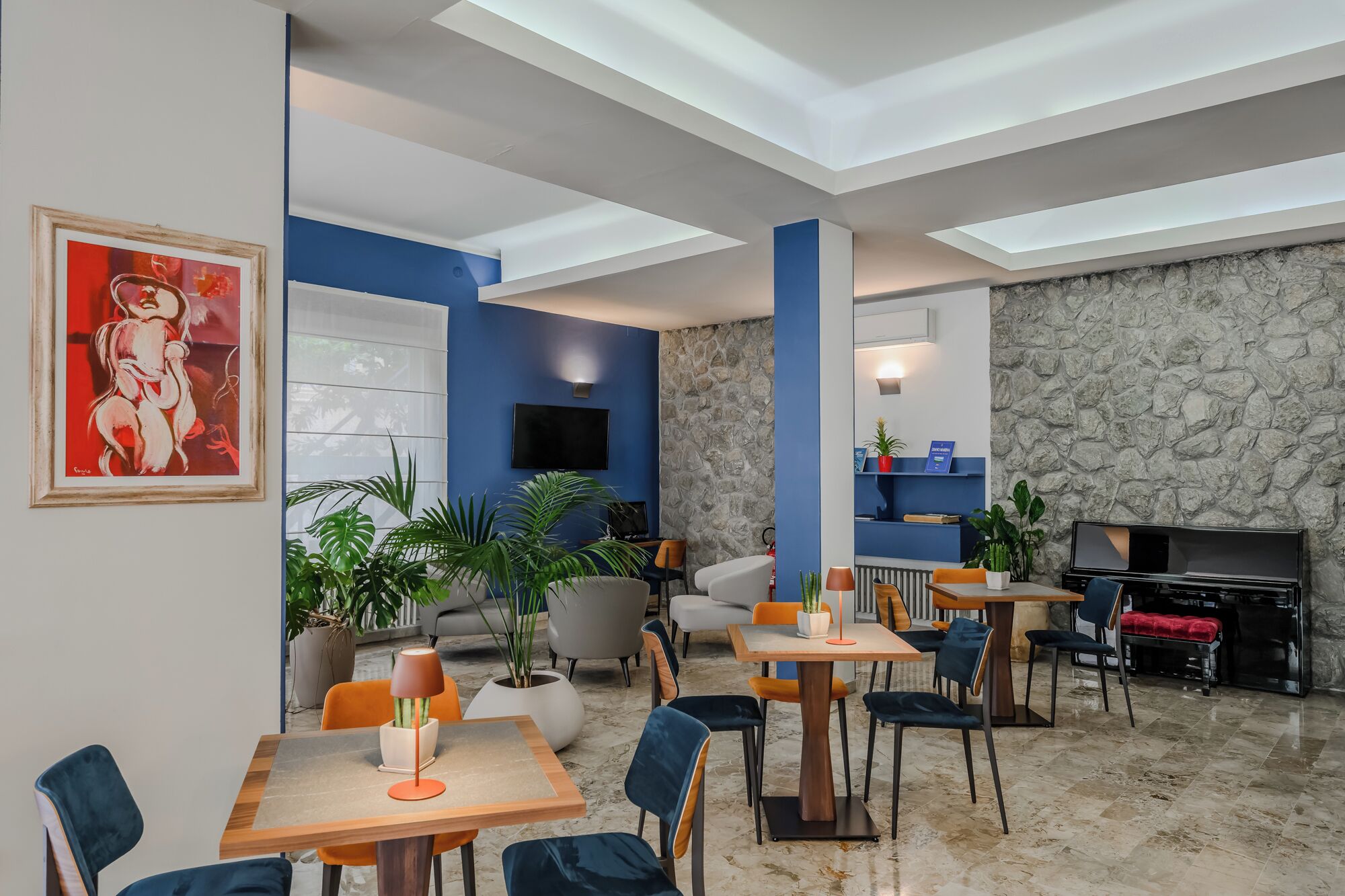 Un moderno hall de hotel con pared de piedra, detalles en azul, un televisor de pantalla plana y una chimenea.
