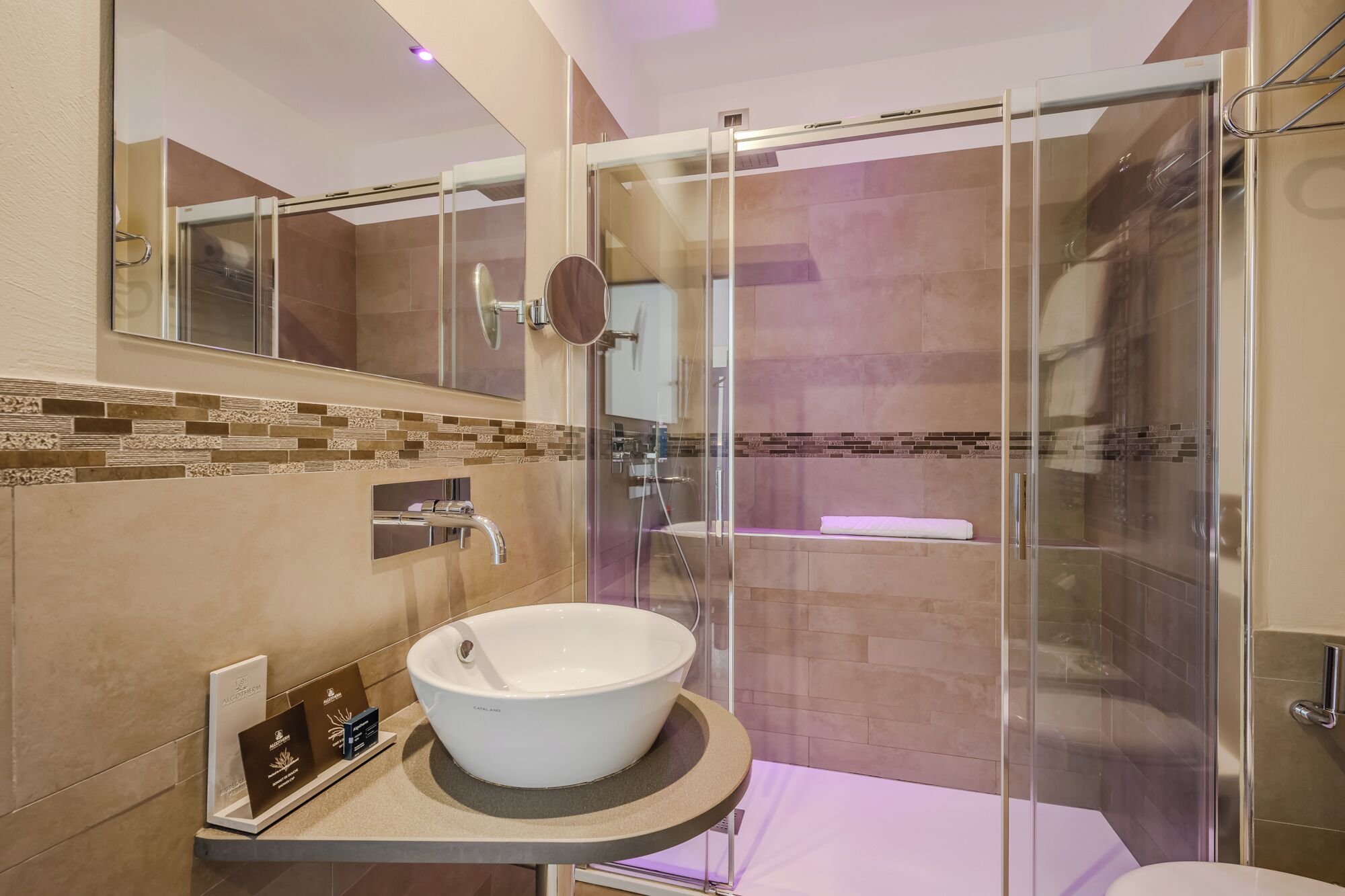 Un baño moderno con ducha envuelta en vidrio, un lavamanos grande de color blanco y un salpicadero de azulejos.