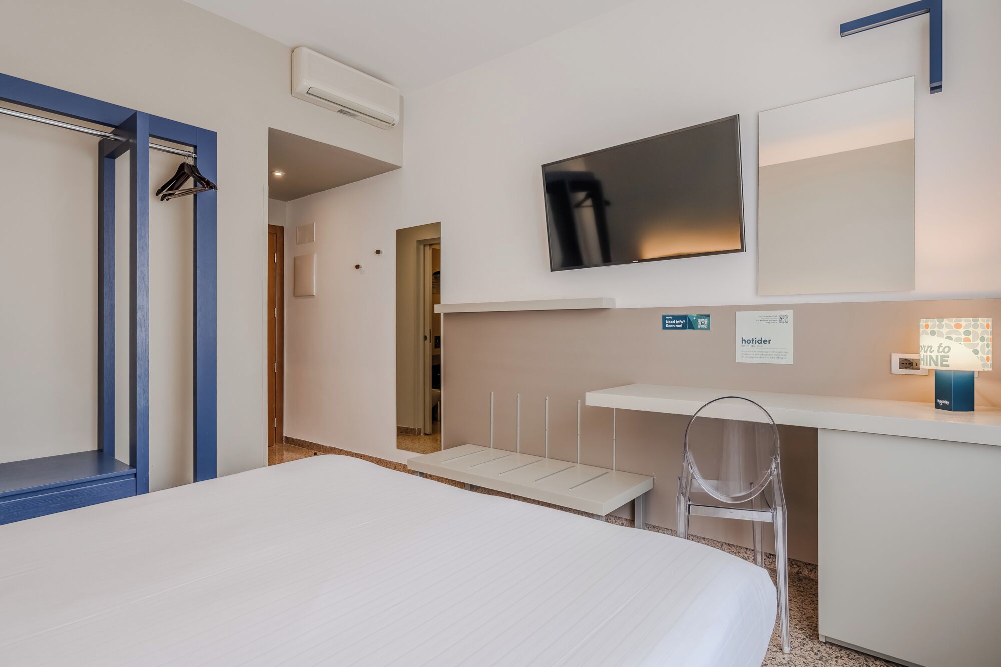 Una habitación de hotel con cama, escritorio, silla, televisión y aire acondicionado.
