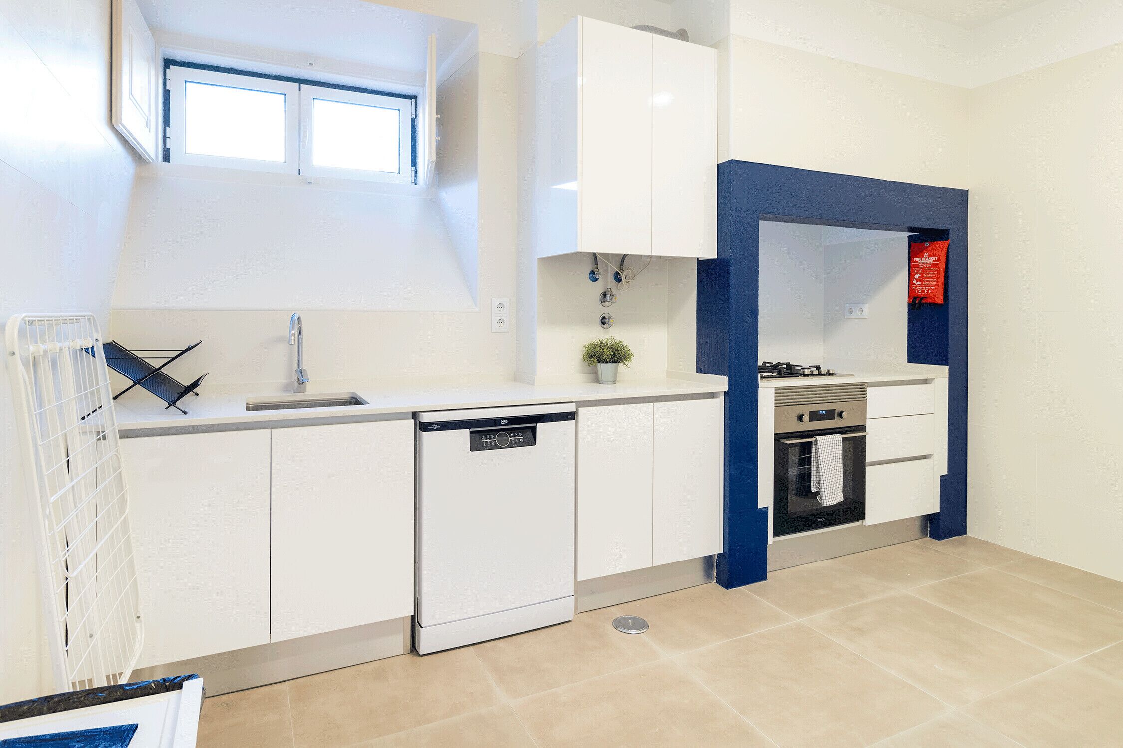 A modern kitchen with white cabinetry, a dishwasher, an oven, and a window above the sink.