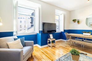 Una sala de estar con un sofá, un televisor, una mesa de comedor y vistas por una ventana.