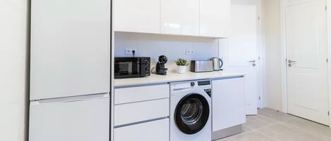 Une cuisine compacte équipée d’un lave-linge, d’un four à micro-ondes et d’une machine à café.