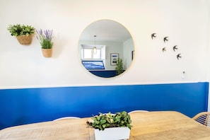 Un comedor con una mesa de madera, una maceta blanca con plantas verdes y un espejo redondo en la pared.