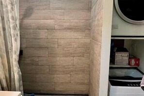 A laundry room with a wooden wall, a washing machine, and a shelf with items.