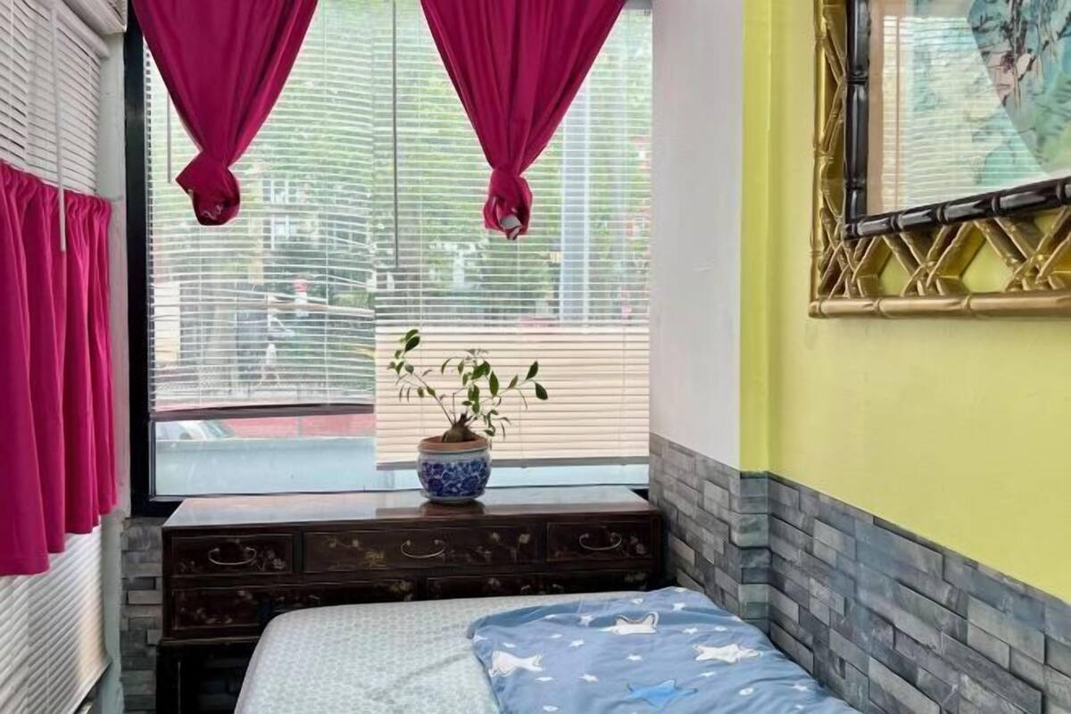 A bedroom with a bed, a window with blinds, a potted plant, and a decorative wall piece.
