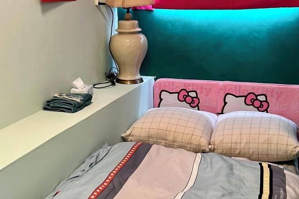 A bed with Hello Kitty bedding, a lamp, and a shelf with folded clothes and a tissue box.