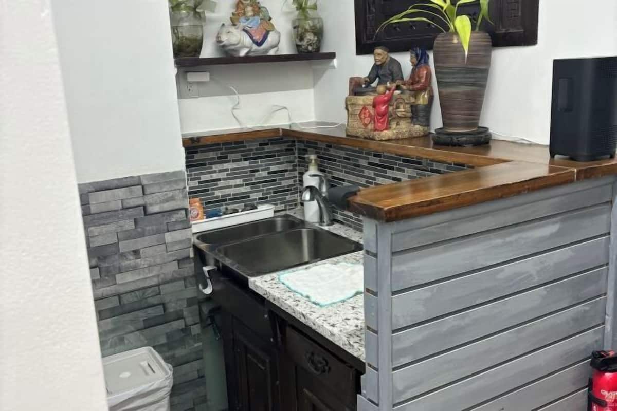 A kitchen with a granite countertop, a stainless steel sink, and a small trash bin.
