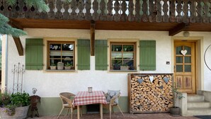 A rustic building with green shutters, a wooden door, and a covered patio area with a table and chairs. - Apartment 'Haus Dekostüble' with Mountain View, Private Terrace and Wi-Fi (Münstertal)