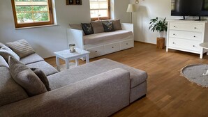 A living room with a sofa, a white cabinet, a television, and a window with a view of trees. - Apartment 'Haus Dekostüble' with Mountain View, Private Terrace and Wi-Fi (Münstertal)