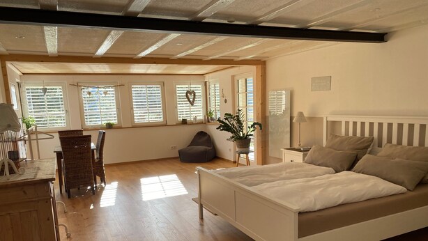 A bedroom with a bed, bedside table, lamp, and a view of the outside through large windows. - Apartment 'Haus Dekostüble' with Mountain View, Private Terrace and Wi-Fi (Münstertal)