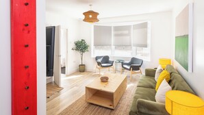 A modern living room with a wooden coffee table, two armchairs, a green sofa, a yellow lamp, and a large window with a view. - Contractor Home Parking & Garden – Near Avonmouth (Bristol)