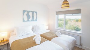 A hotel room with two beds, a window with a view, a bedside table with a lamp, and abstract wall art. - Contractor Home Parking & Garden – Near Avonmouth (Bristol)