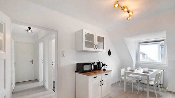 A modern kitchen with white cabinetry, a dining area with white chairs, and a window providing natural light. - Entire 'Hallerstraße' Unit with 4 Apartments, Balcony and Wi-Fi (Pforzheim)