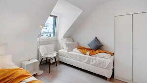 A modern bedroom with a sloped ceiling, a white bed, a chair, a radiator, and a wardrobe. - Entire 'Hallerstraße' Unit with 4 Apartments, Balcony and Wi-Fi (Pforzheim)