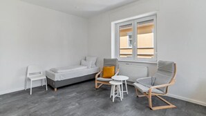A room with a bed, two chairs, a small table, and a window with blinds. - Entire 'Hallerstraße' Unit with 4 Apartments, Balcony and Wi-Fi (Pforzheim)