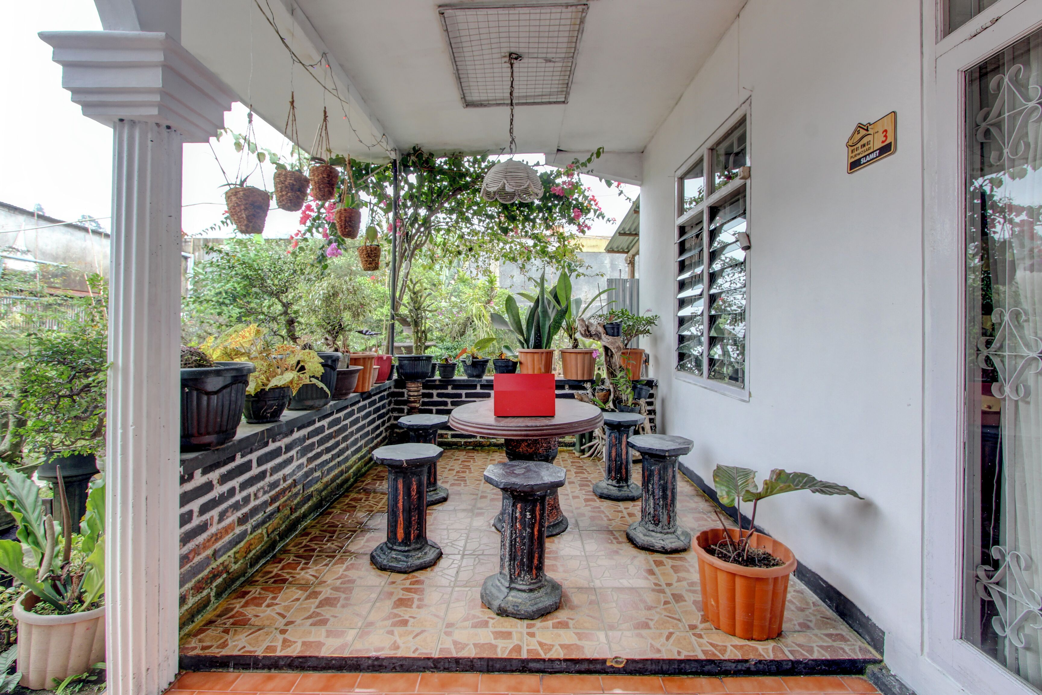 Un espace extérieur abrité, agrémenté de plantes en pot, d’une table ronde et de tabourets en pierre.