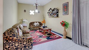 A living room with a patterned sofa, a coffee table, a decorative vase, and a wall-mounted shelf. - OYO 94841 Alodia Homestay Family (Kejajar)