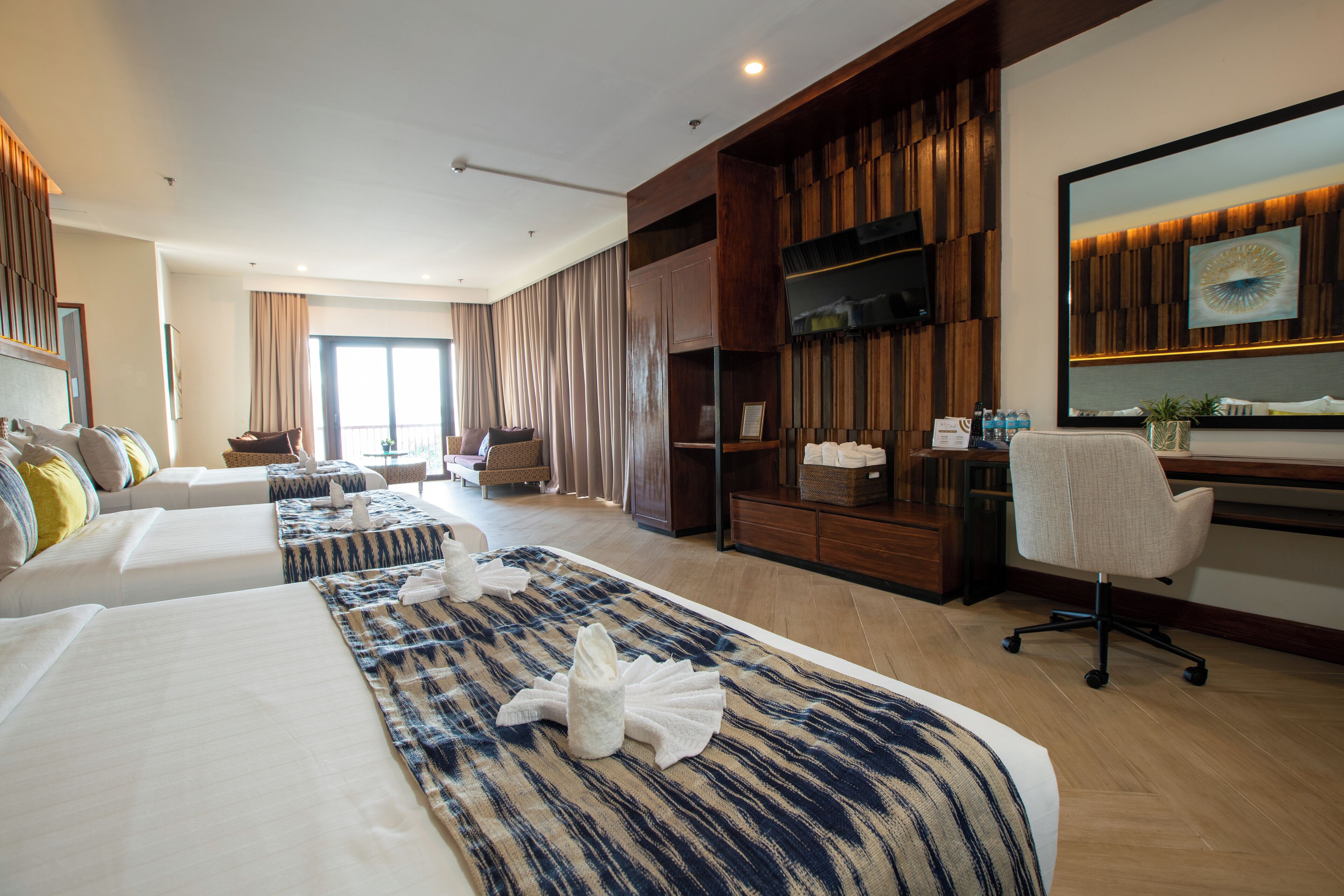Habitación de hotel con dos camas, un escritorio, una silla, un televisor y un ventanal grande.