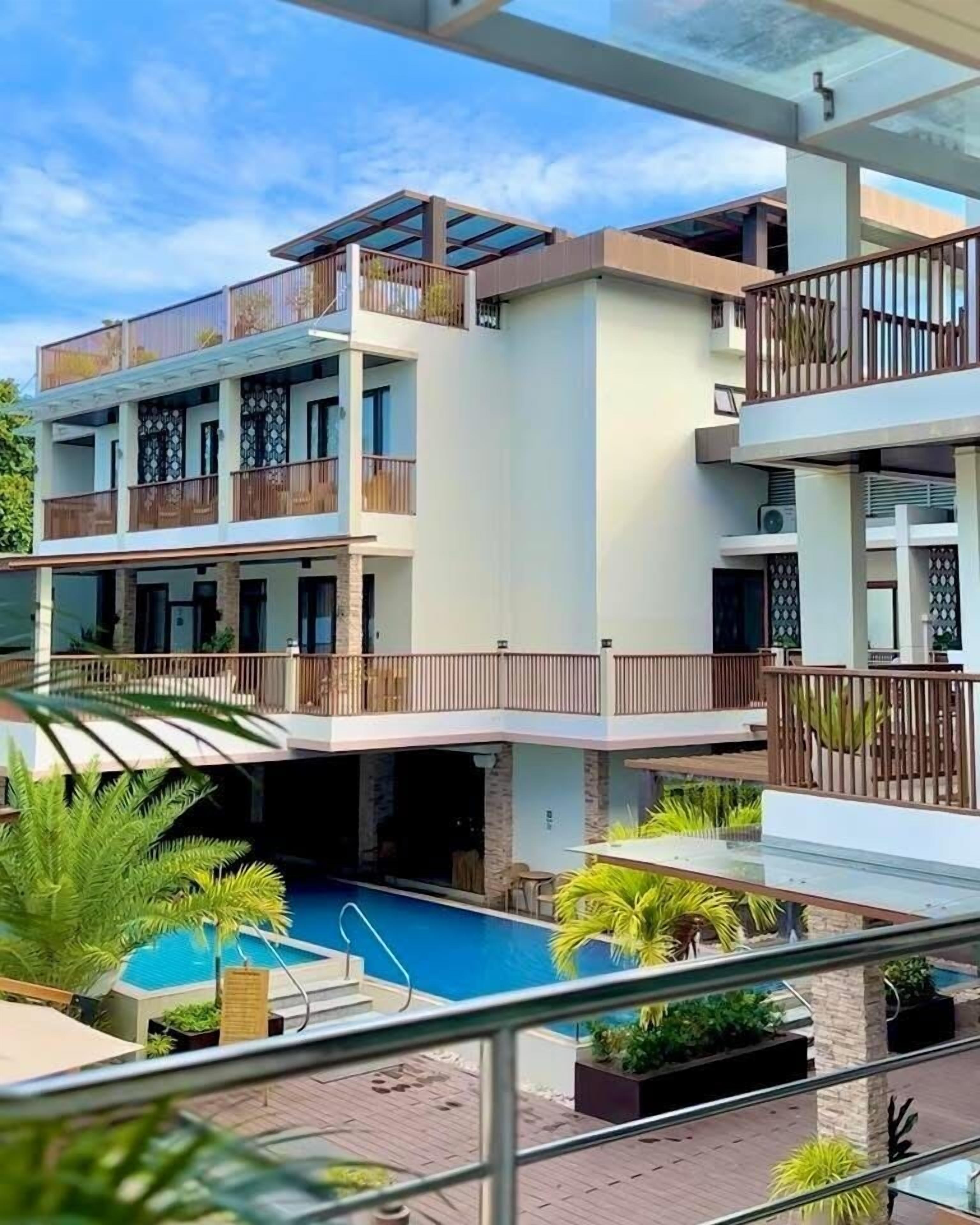 A multi-story hotel with balconies, a swimming pool, and outdoor seating areas.