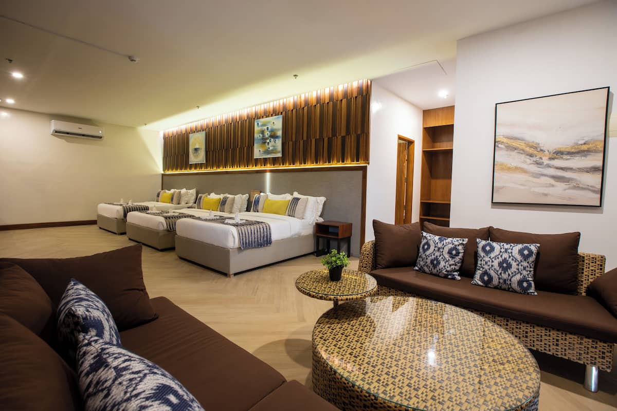 A modern hotel room with a large bed, a sofa, a round coffee table, and a wall-mounted TV.