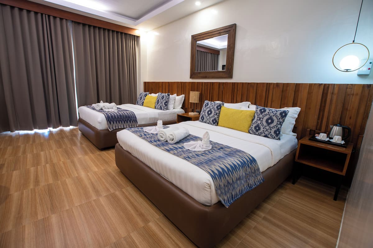 A hotel room with two beds, wooden headboards, a mirror, a bedside table with a lamp, and a tray with a coffee pot.
