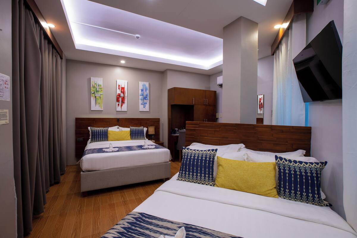 A hotel room with two beds, wooden headboards, and a flat-screen TV mounted on the wall.