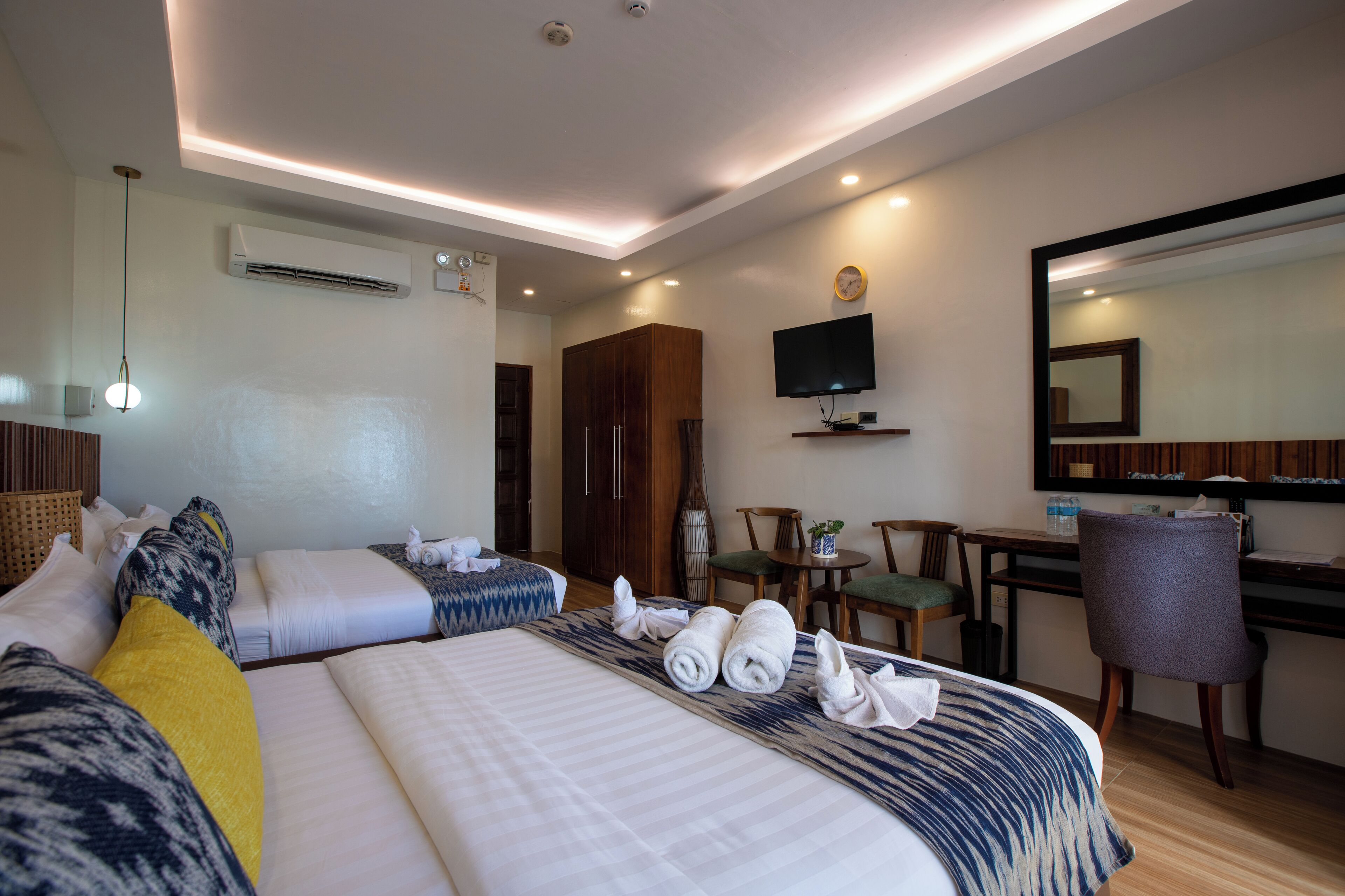 A hotel room with two beds, a desk, a chair, a TV, and an air conditioning unit.