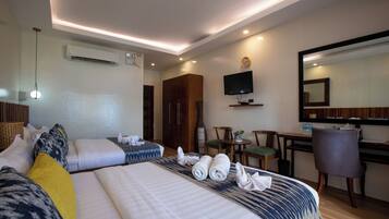 A hotel room with two beds, a desk, a chair, a TV, and an air conditioning unit.
