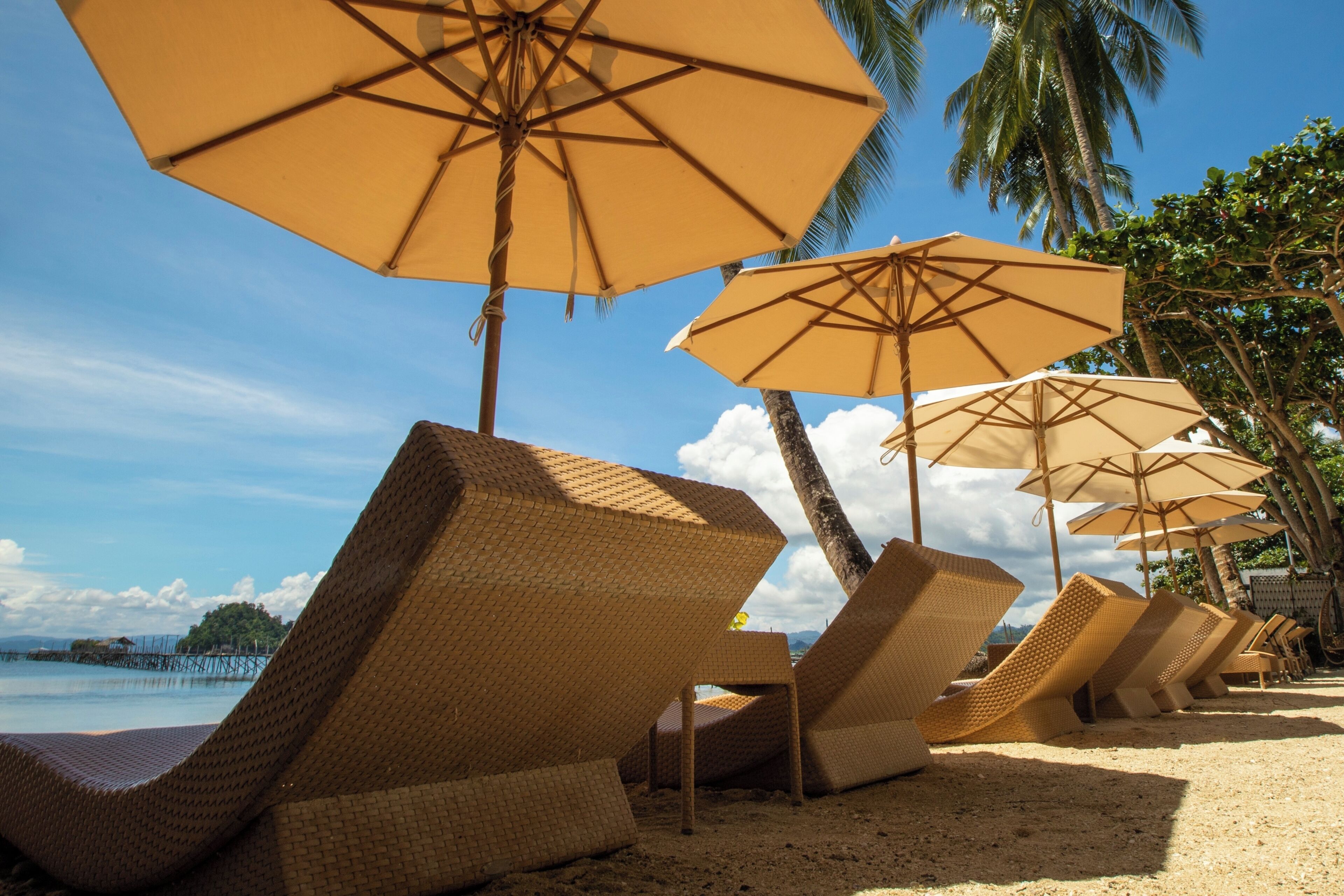 Una playa con sillones de mimbre y sombrillas color beige.