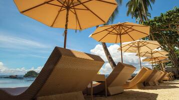 Una playa con sillones de mimbre y sombrillas color beige.