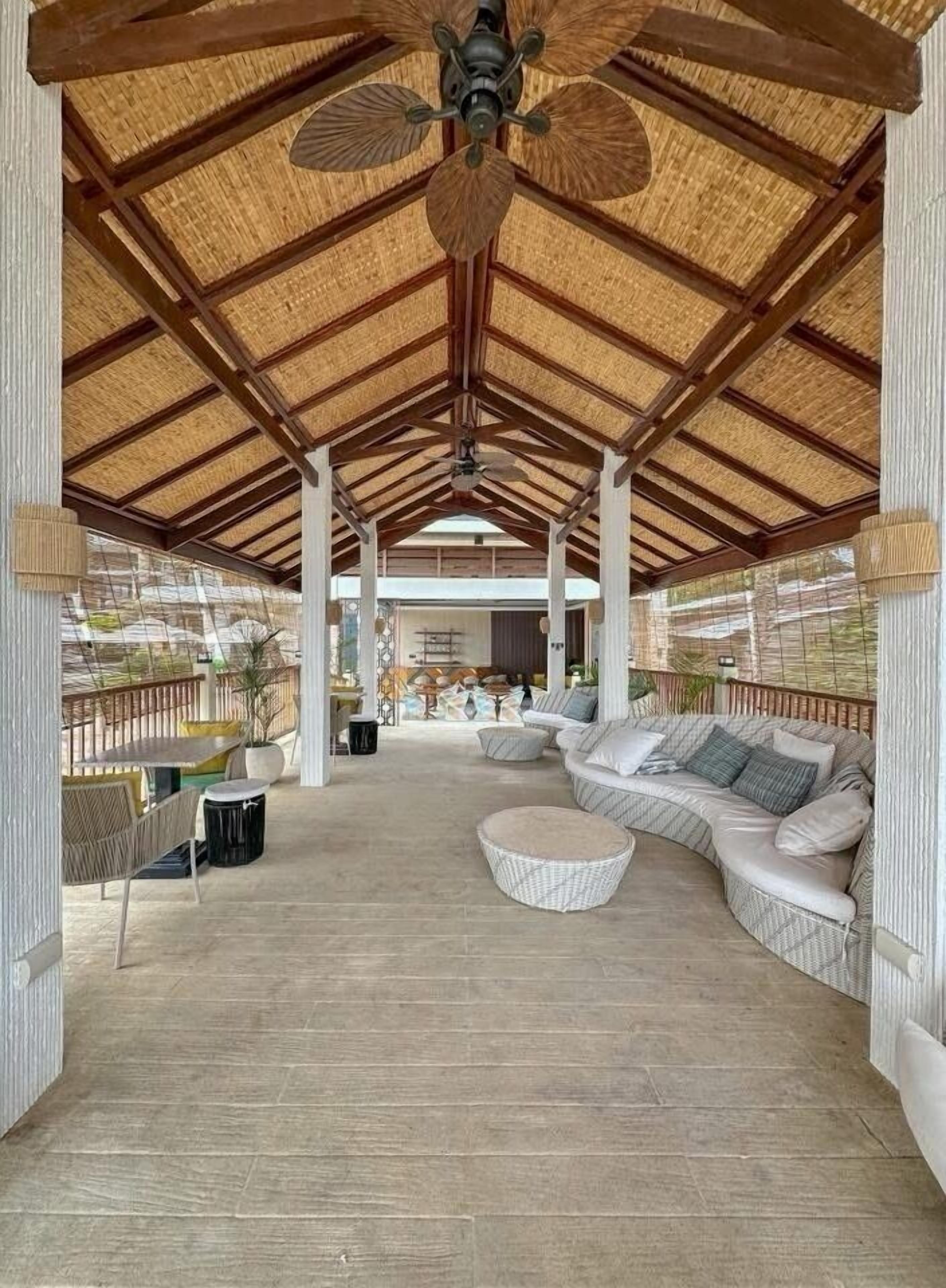 An open-air covered patio with a high ceiling, a large sofa, and a ceiling fan.
