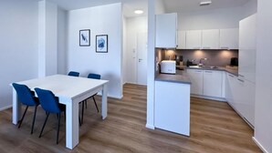 A modern kitchen with white cabinets, a central island, and a dining area with a white table and blue chairs. - SUITE4ME - Balcony I Kitchen I Washing machine I Mainz-Kostheim (Wiesbaden)