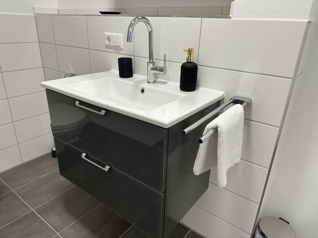 A modern bathroom with a white sink, black cabinet, and a towel rack.