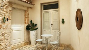 A small outdoor seating area with two metal chairs and a table, a potted plant, and a door with a number plate. - Borgo Sant' Angelo exclusive house Room 1 (Conversano)